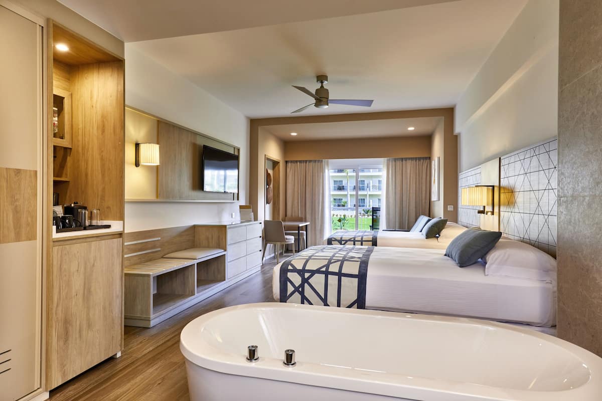 Une chambre d’hôtel avec une grande baignoire, un bureau, une chaise, un lit et une vue sur l’extérieur.