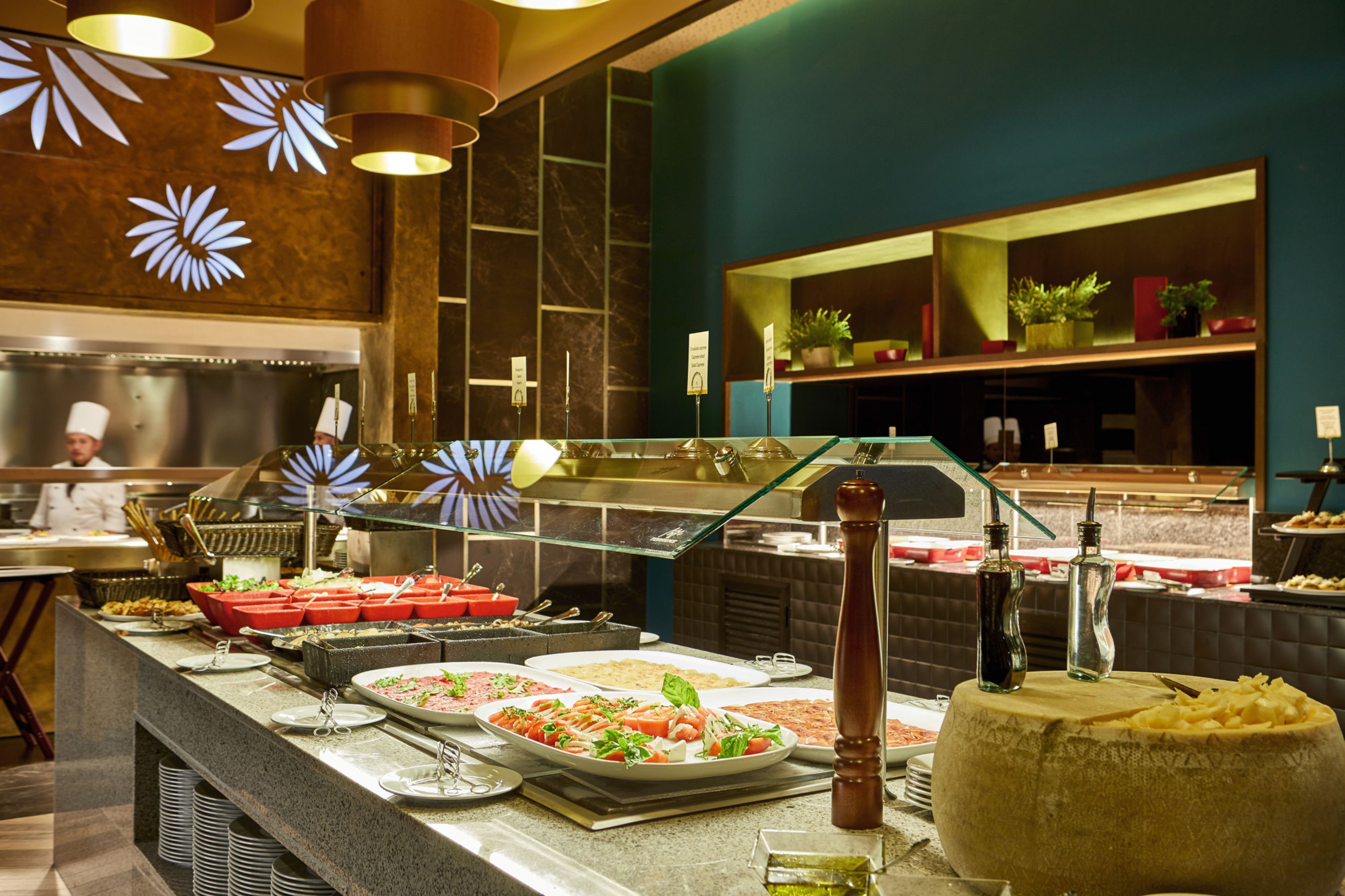 A buffet with various food items, a chef in the background, and a modern interior design.