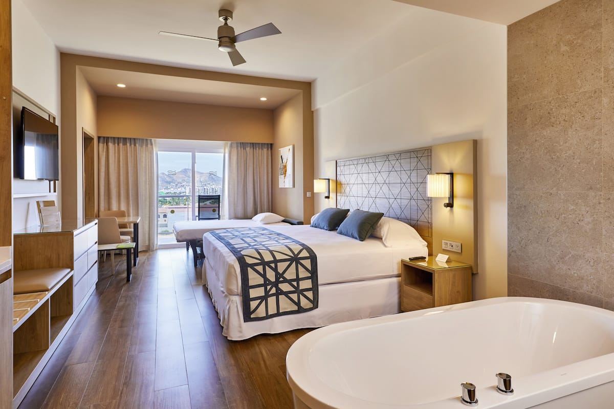 Une chambre d’hôtel avec un grand lit, une baignoire, un bureau avec une chaise, une télévision et une vue sur la ville.