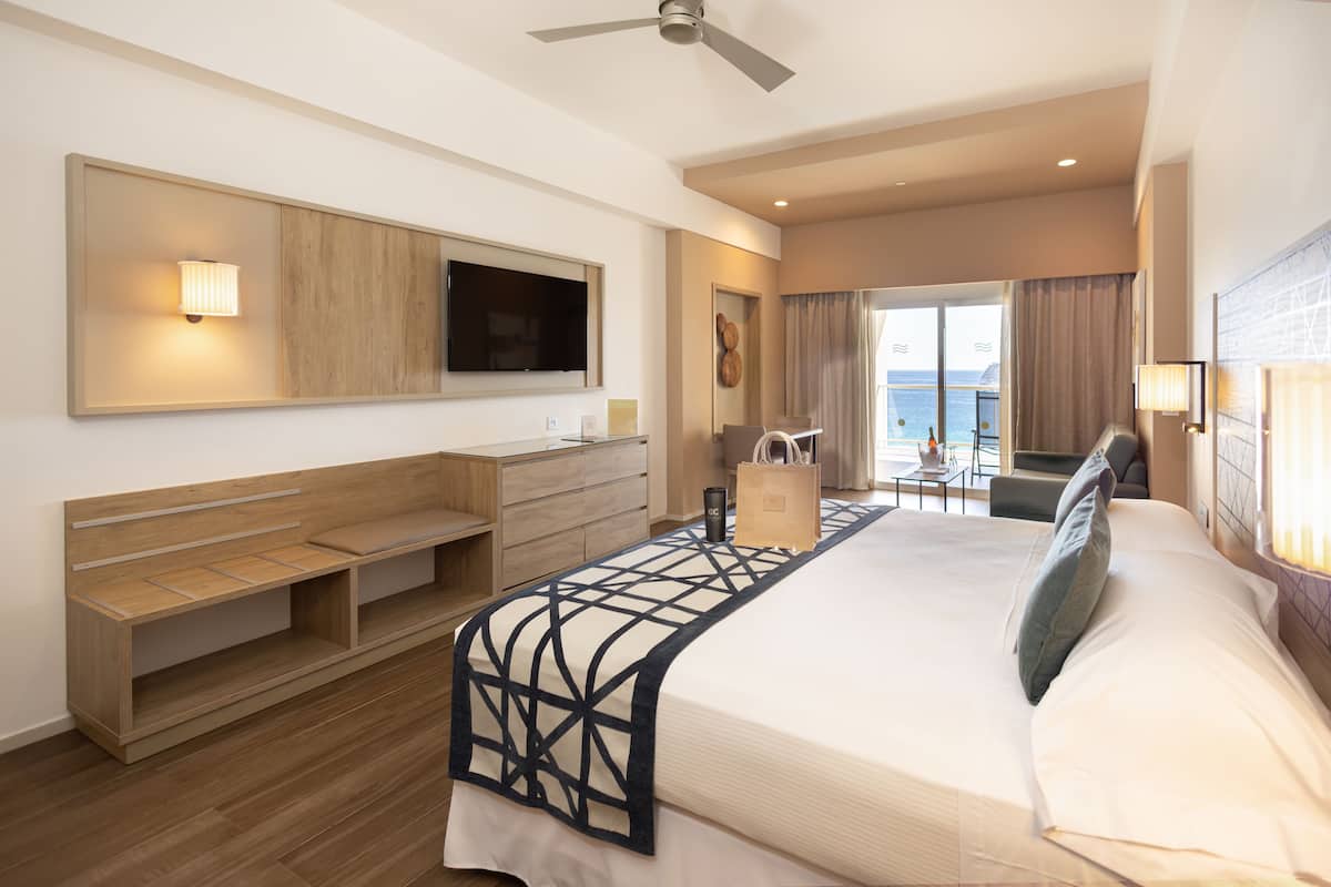 Une chambre d’hôtel moderne dotée d’un grand lit, d’une télévision, d’un bureau et d’un balcon offrant une vue sur la mer.