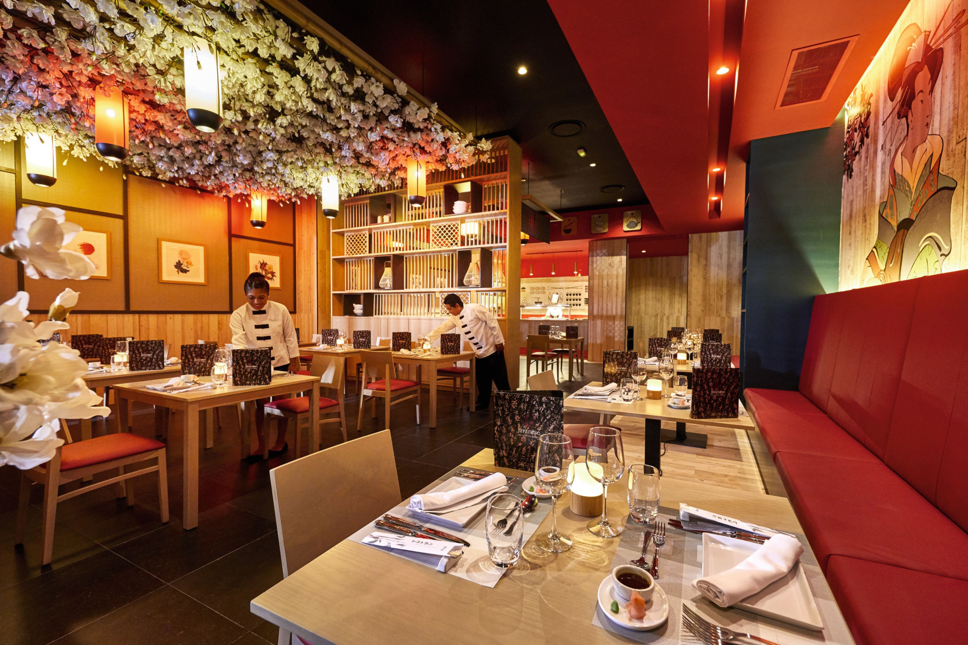 A restaurant with wooden tables and chairs, floral decorations on the ceiling, and a red cushioned bench.