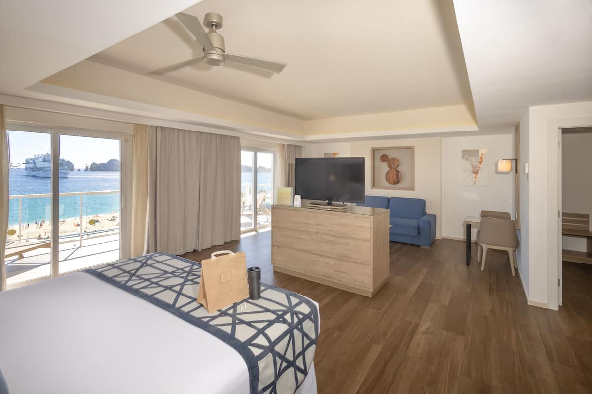 Une chambre d’hôtel avec un lit, un bureau, une télévision, un canapé et une vue sur la mer.