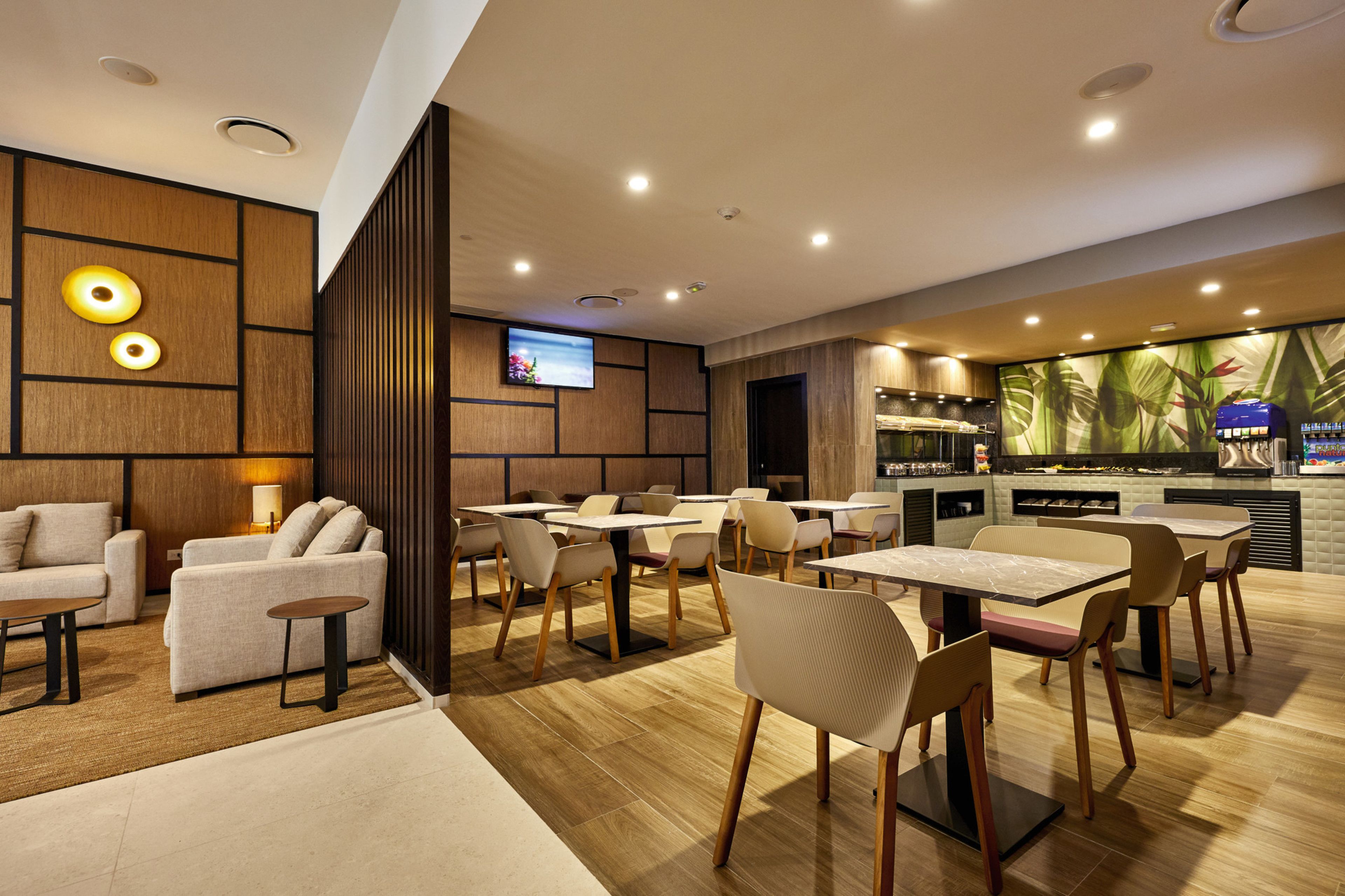 Un restaurante moderno con paneles de madera, luces empotradas en el techo y una televisión de pantalla plana. Mesas y sillas dispuestas para comer.