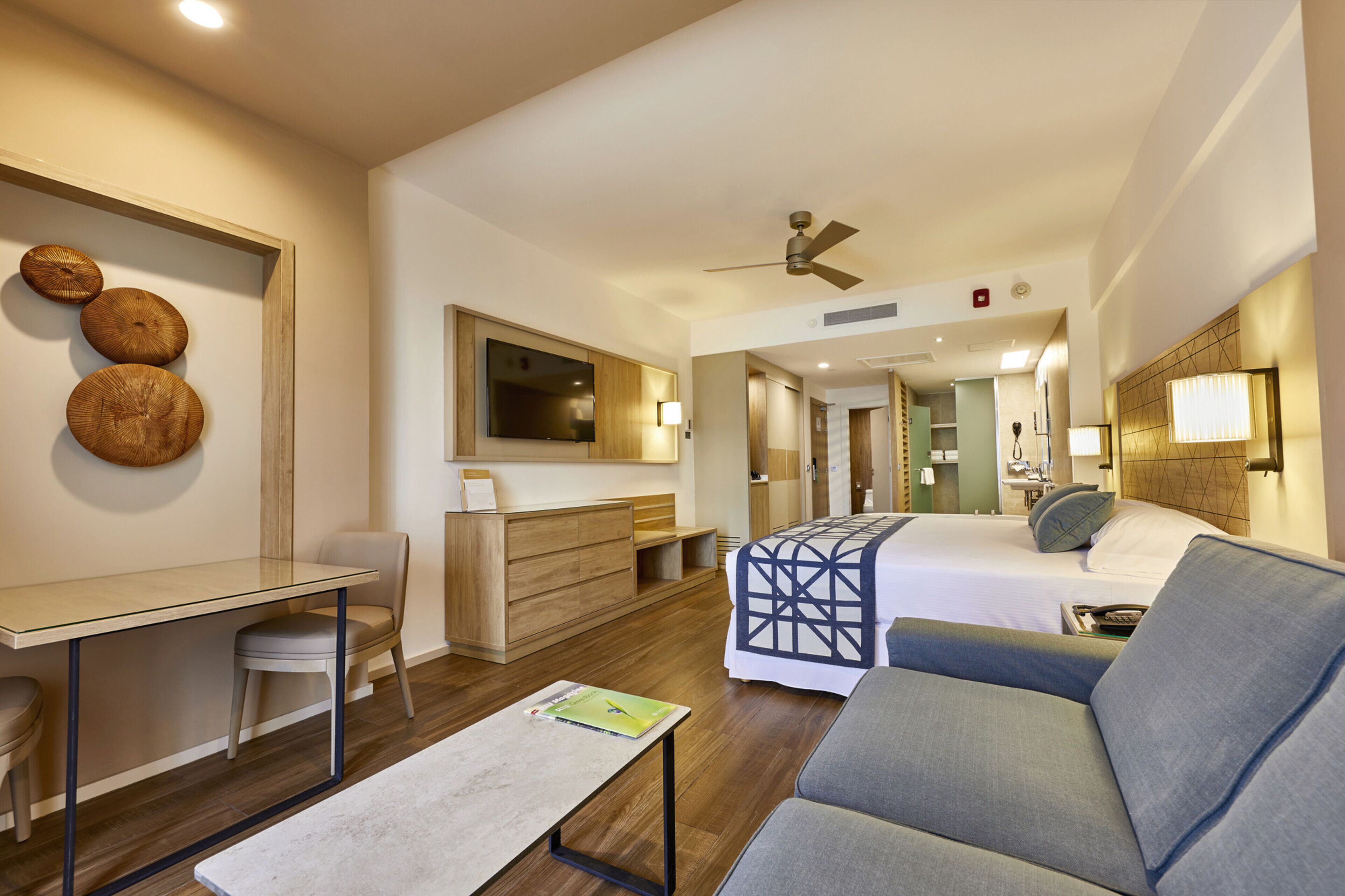 A modern hotel room with a bed, a sofa, a desk, and a chair.
