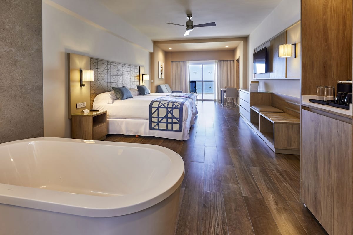 Une chambre d’hôtel avec une grande baignoire, deux lits, un balcon avec vue et une kitchenette.