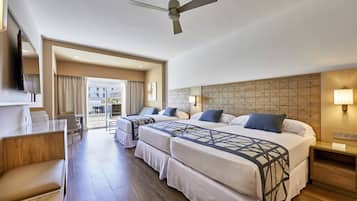 A hotel room with two beds, a desk, a chair, a TV, and a ceiling fan.
