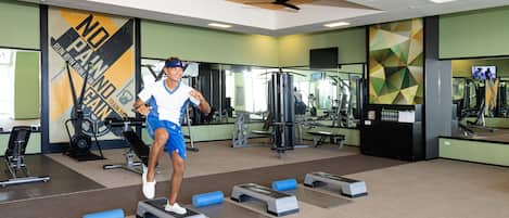 A gym with exercise equipment, mirrors, and a motivational wall.