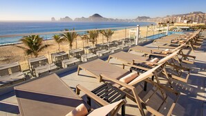 Zona d'oci al terrat amb gandules i piscina, amb vista a una platja i muntanyes.
