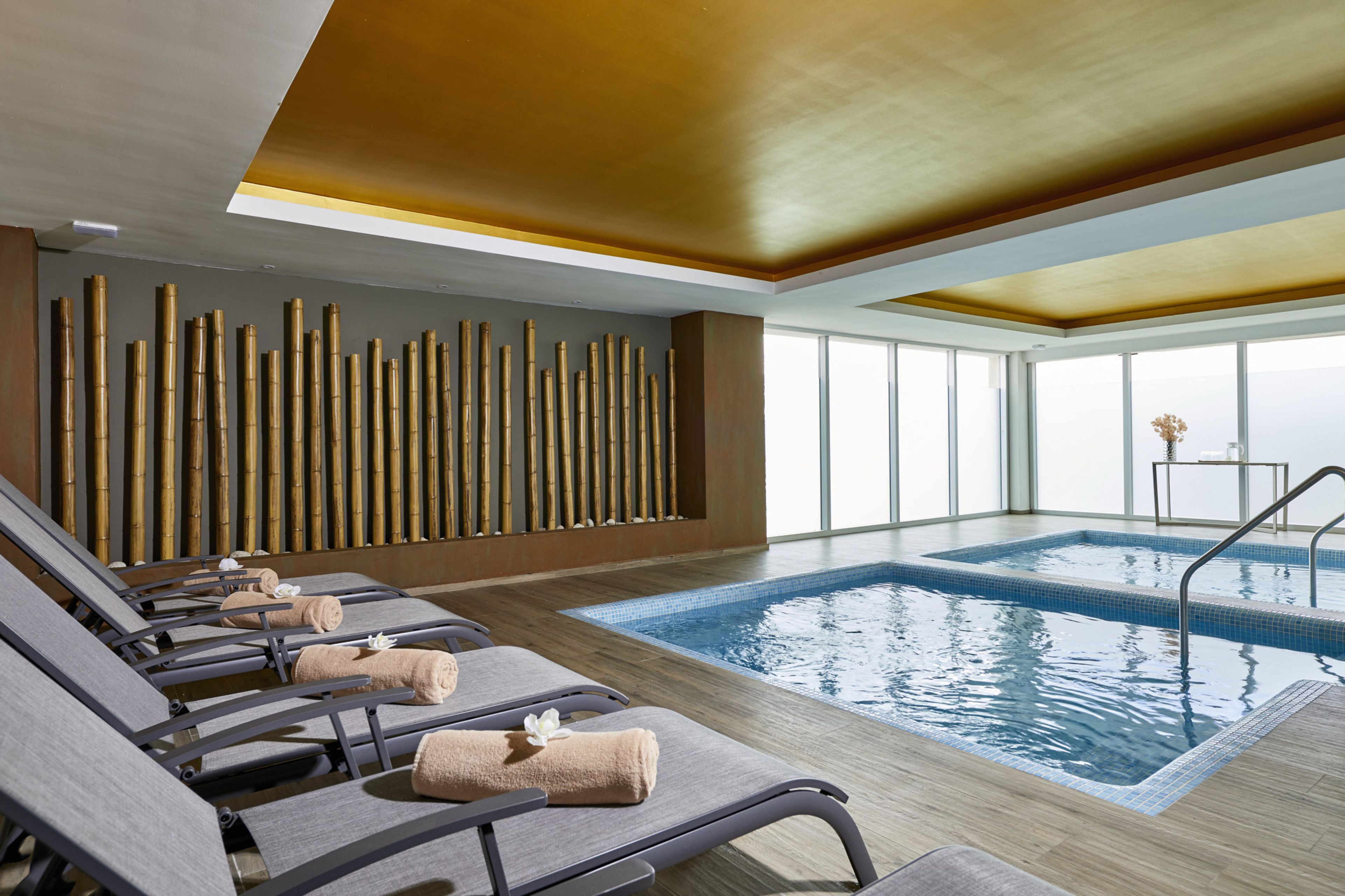 Un área de piscina interior moderna con sillones reclinables y una pared de bambú.