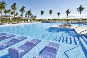 A swimming pool with clear blue water, lounge chairs, and palm trees.