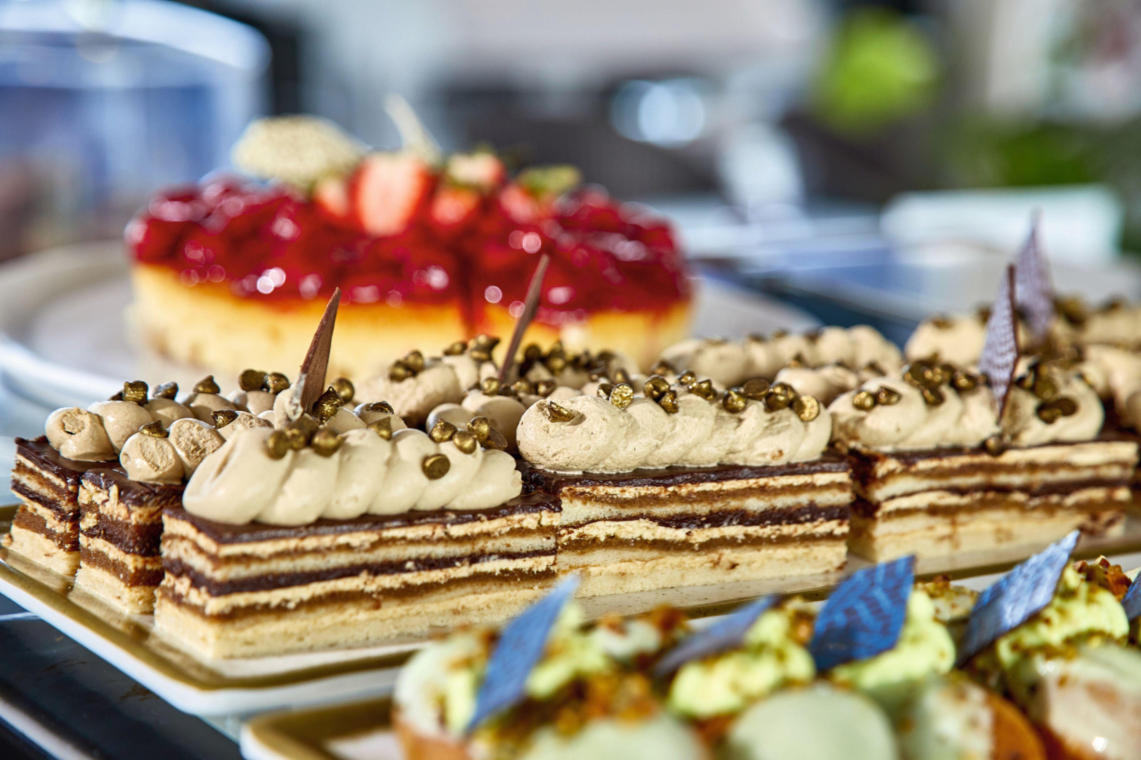 A variety of desserts on a tray, including a layered cake with cream and nuts, and a cake with red fruit topping.