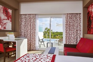Habitación de hotel con cama, escritorio, silla, sofá y vista a una piscina y palmeras.