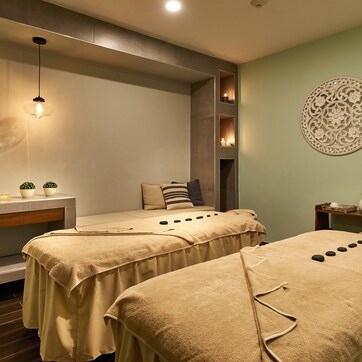 A spa room with two massage tables, a sink, a mirror, and decorative wall art.