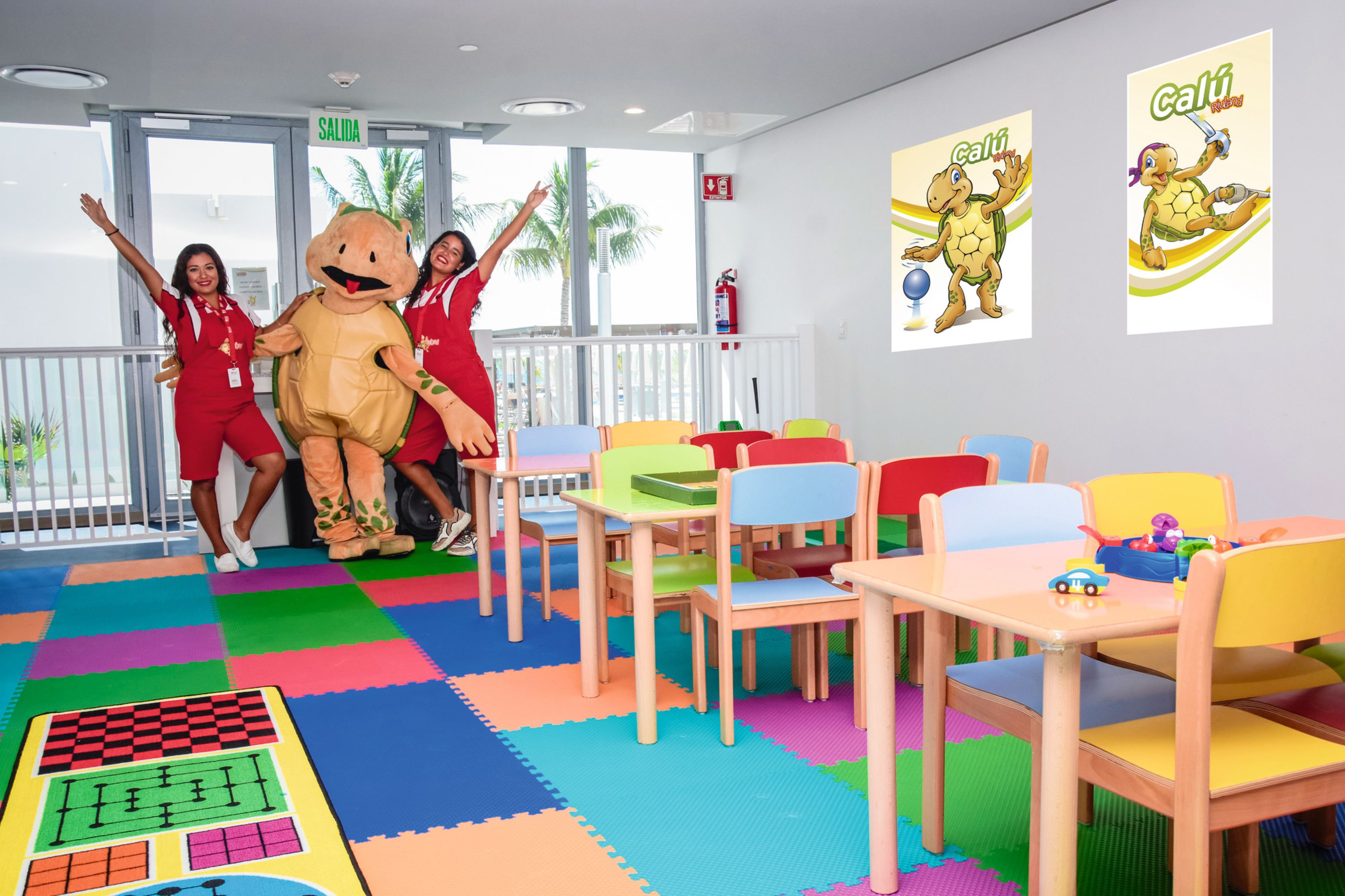 Un salón de juegos de colores vivos con un personaje promocional, un extintor y un letrero que indica 'SALIDA'.