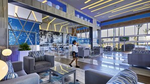 A spacious lobby with modern furniture, a large digital display, and a view of the outdoors. - Hotel Riu Palace Costa Mujeres - All Inclusive (Costa Mujeres)