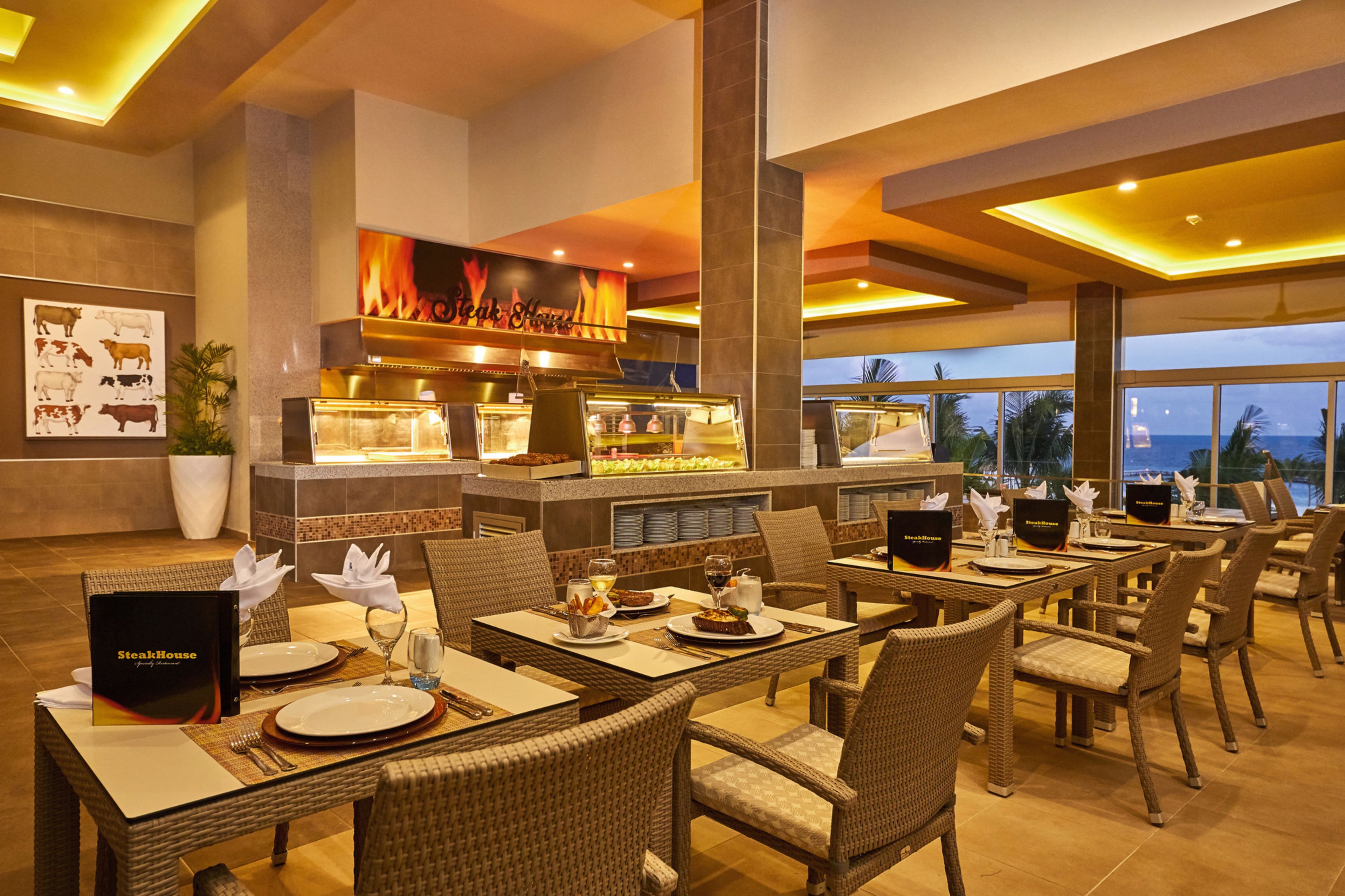 A restaurant with a view of the ocean, featuring wicker chairs, a buffet, and a menu stand.