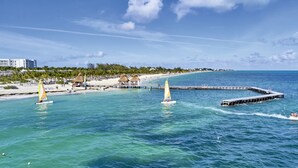 A beach scene with clear turquoise waters, a pier, and a thatched-roof structure. - Hotel Riu Palace Costa Mujeres - All Inclusive (Costa Mujeres)