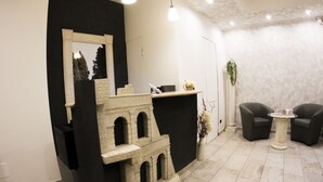 A reception area with a stone counter, a mirror, and a seating area with two chairs and a small table. - Mirabilia Guest House (Rome)