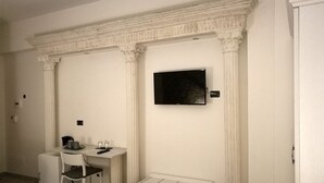 A room with a white desk, a chair, a small table, and a television mounted on the wall. - Mirabilia Guest House (Rome)