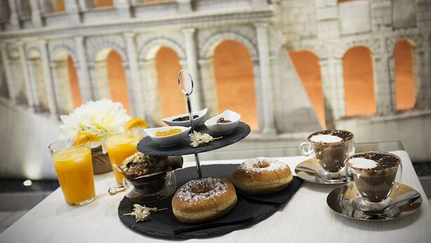 A breakfast setting with a tiered serving tray, two cups of coffee, a glass of orange juice, and a plate with donuts and pastries. - Mirabilia Guest House (Rome)