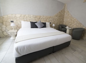 Ein geräumiges Schlafzimmer mit einem großen Bett, einer Steinwand, zwei Nachttischen mit Lampen, einem Sessel und einem kleinen Tisch mit einer Kerze.