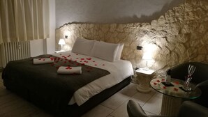 A bedroom with a stone wall, a bed with rose petals, two bedside lamps, and a small table with a glass top. - Mirabilia Guest House (Rome)