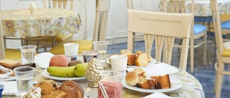 Una mesa de comedor dispuesta con diferentes alimentos y bebidas, rodeada de sillas y un mantel estampado.