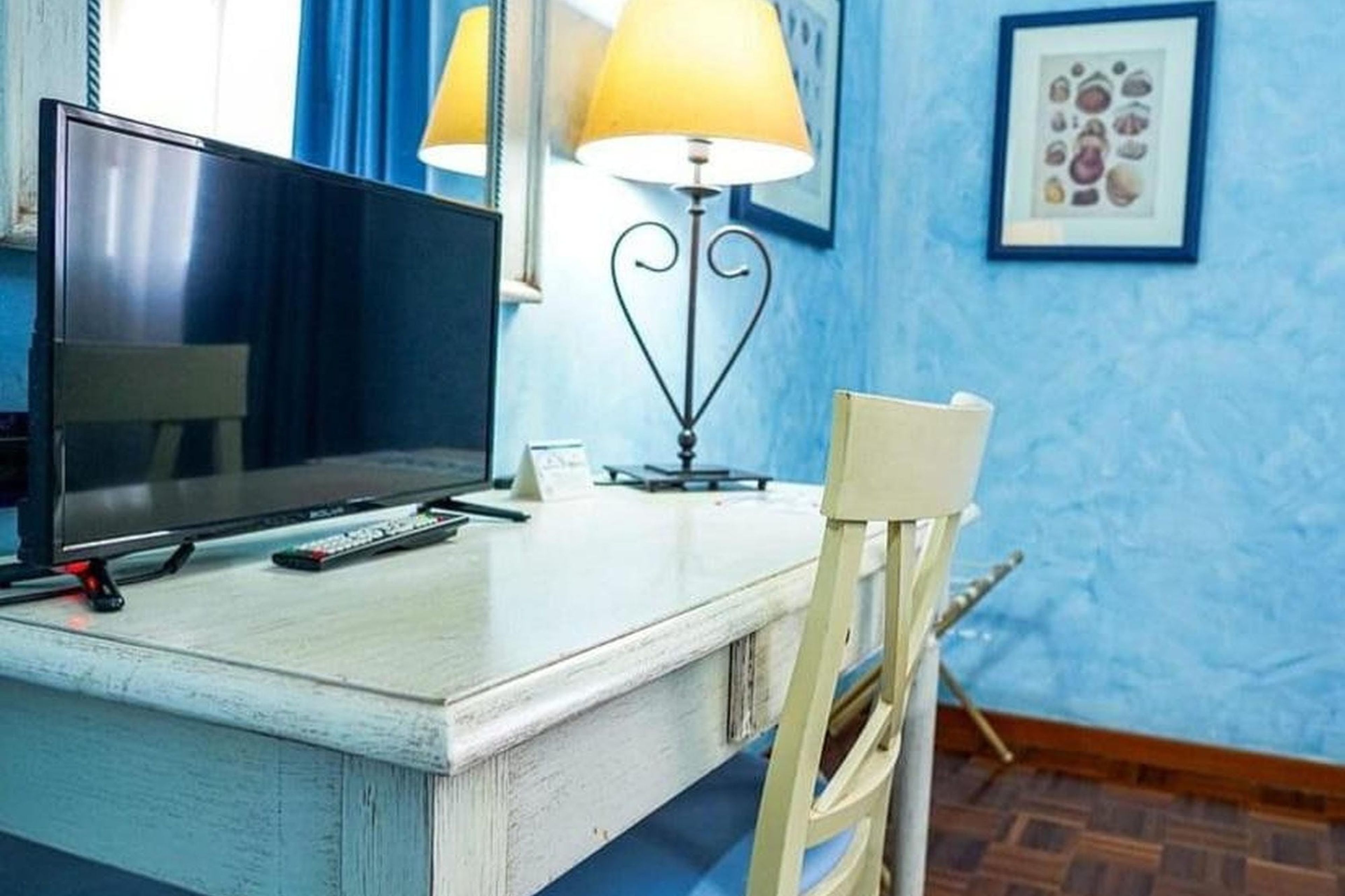 Una camera d'albergo con una scrivania, una televisione, una lampada, una sedia e un quadro appeso al muro.