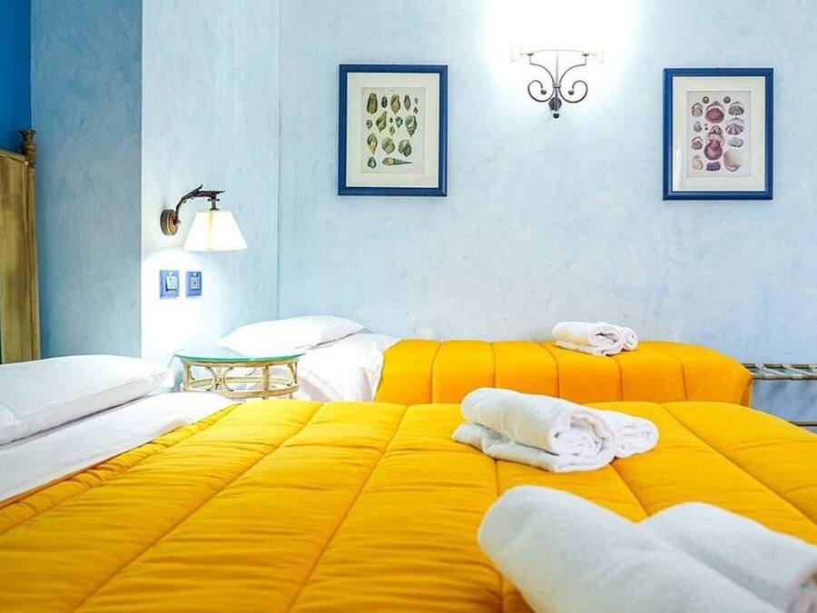 Una camera d'albergo con due letti, un comodino, una lampada e due quadri appesi al muro.
