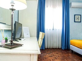 Una stanza con scrivania, computer, lampada, sedia e un letto con cuscino giallo.