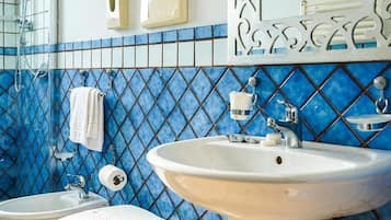 Un baño con un lavabo blanco, dos inodoros, un perchero para toallas y una pared con azulejos azules.