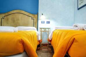 A hotel room with two beds, each with a yellow bedspread and white towels, a wooden headboard, a small table with a lamp, and a blue wall. - Motel - Hotel Nautico Pozzallo (Pozzallo)
