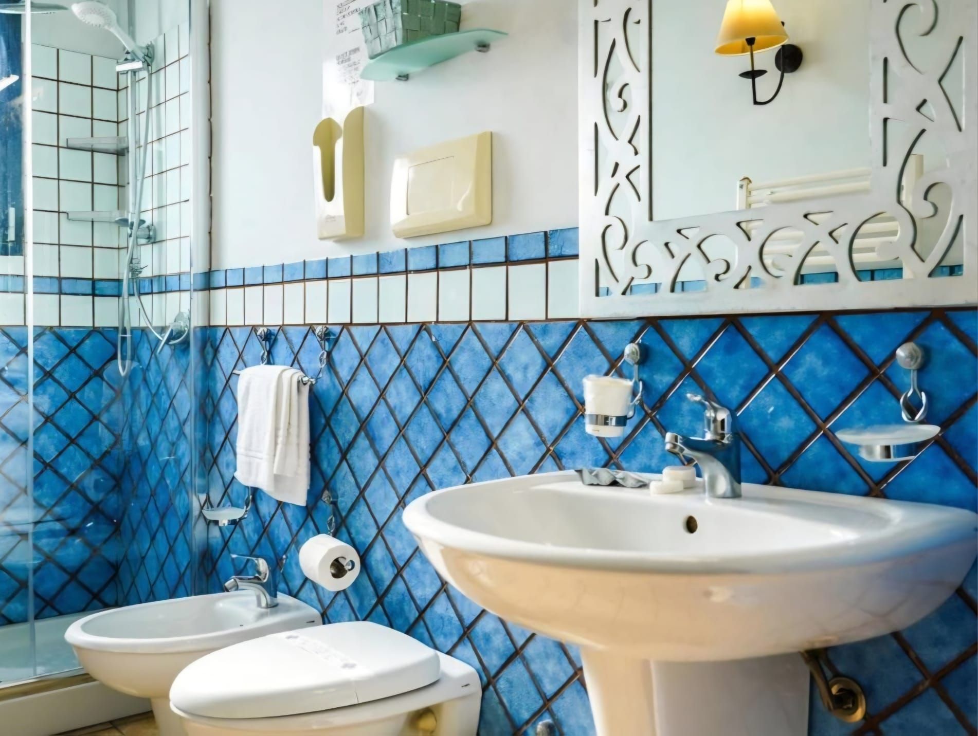 Un baño con un lavamanos blanco, dos inodoros, una ducha y un espejo con un marco decorativo.