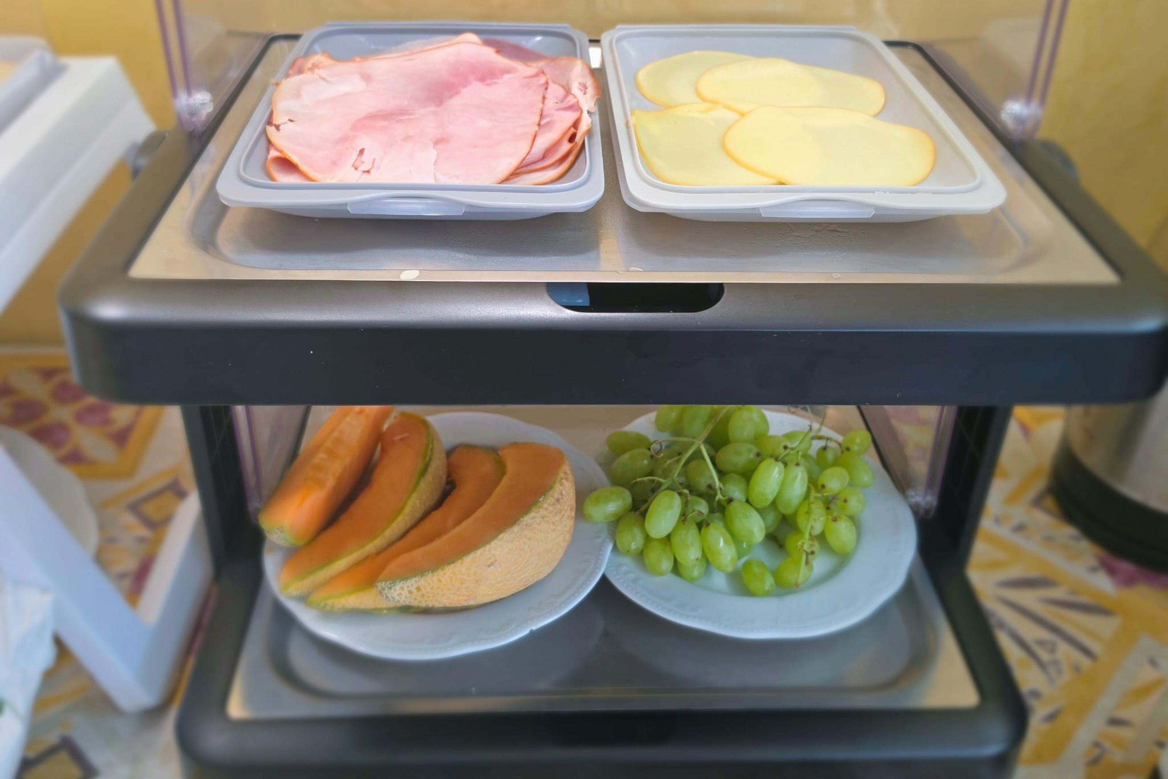 Un carro de servicio de alimentos con jamón, queso, pan y uvas.