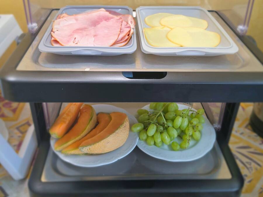Un chariot de service contenant du jambon, du fromage, du pain et des raisins.