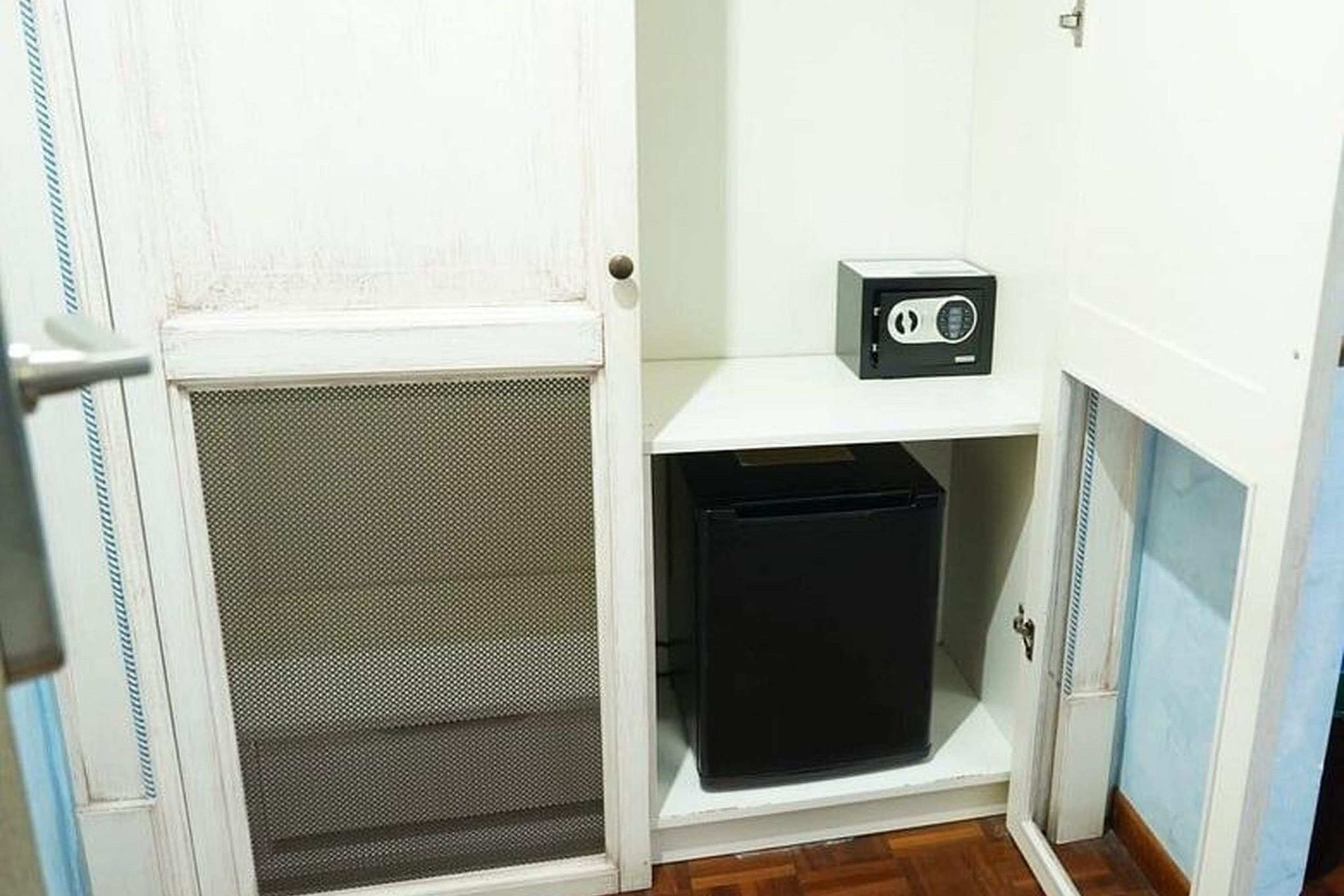 Una habitación pequeña con una puerta blanca, un mueble de almacenaje negro y un estante blanco con una radio.