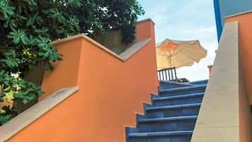 Una escalera con barandilla azul y paredes anaranjadas que lleva a una zona techada con un paraguas.