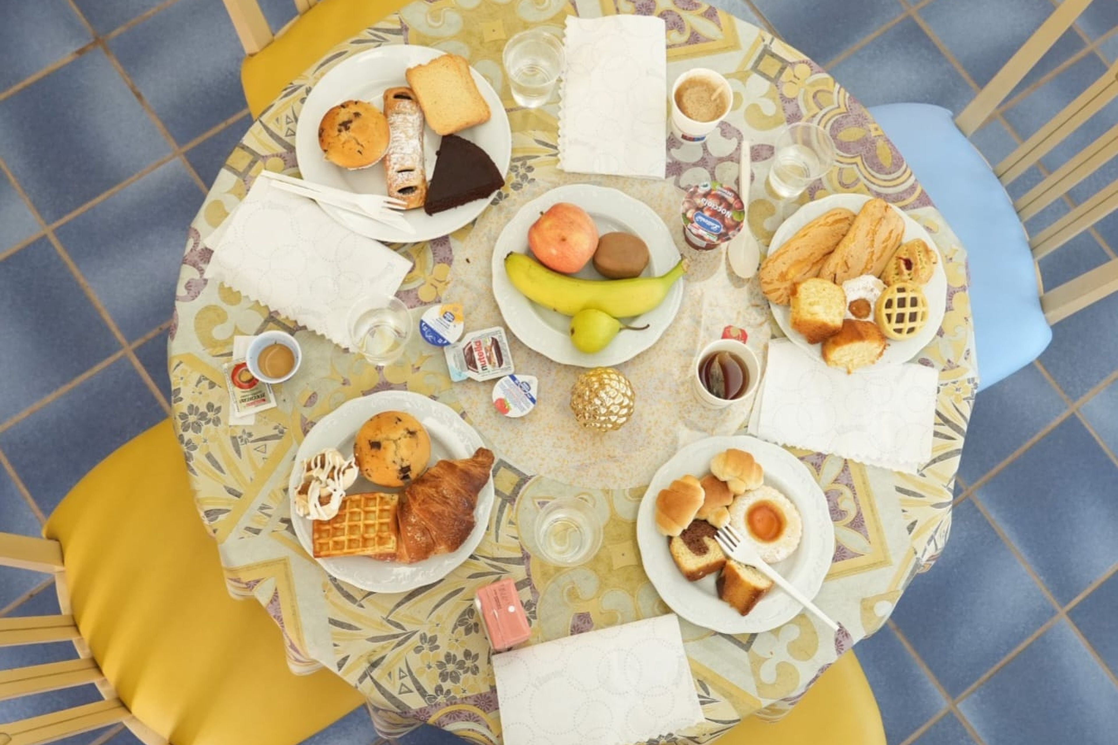 Una mesa redonda con diversos alimentos y bebidas, rodeada de sillas amarillas y azules.