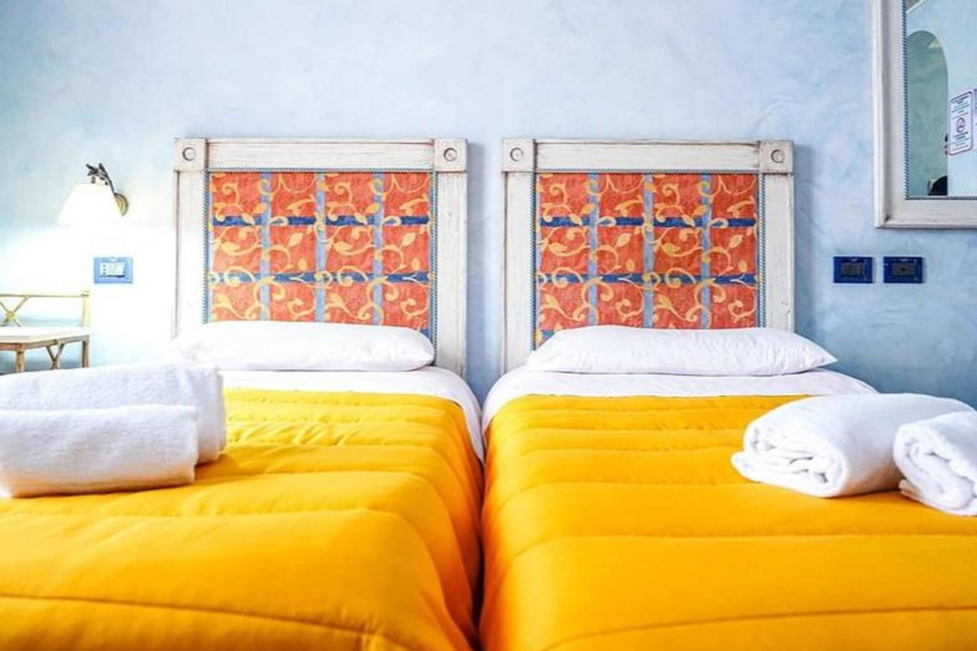 Habitación de hotel con dos camas, cada una con cabecera estampada y ropa de cama amarilla.