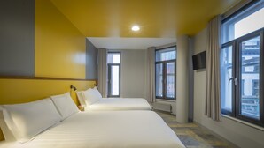 Ein Hotelzimmer mit zwei Betten, großen Fenstern, einem Flachbildfernseher und einer Deckenleuchte.