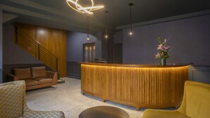 Ein Empfangsbereich mit einem Holzbüro, einer Treppe, einem Sofa und einem gelben Sessel.