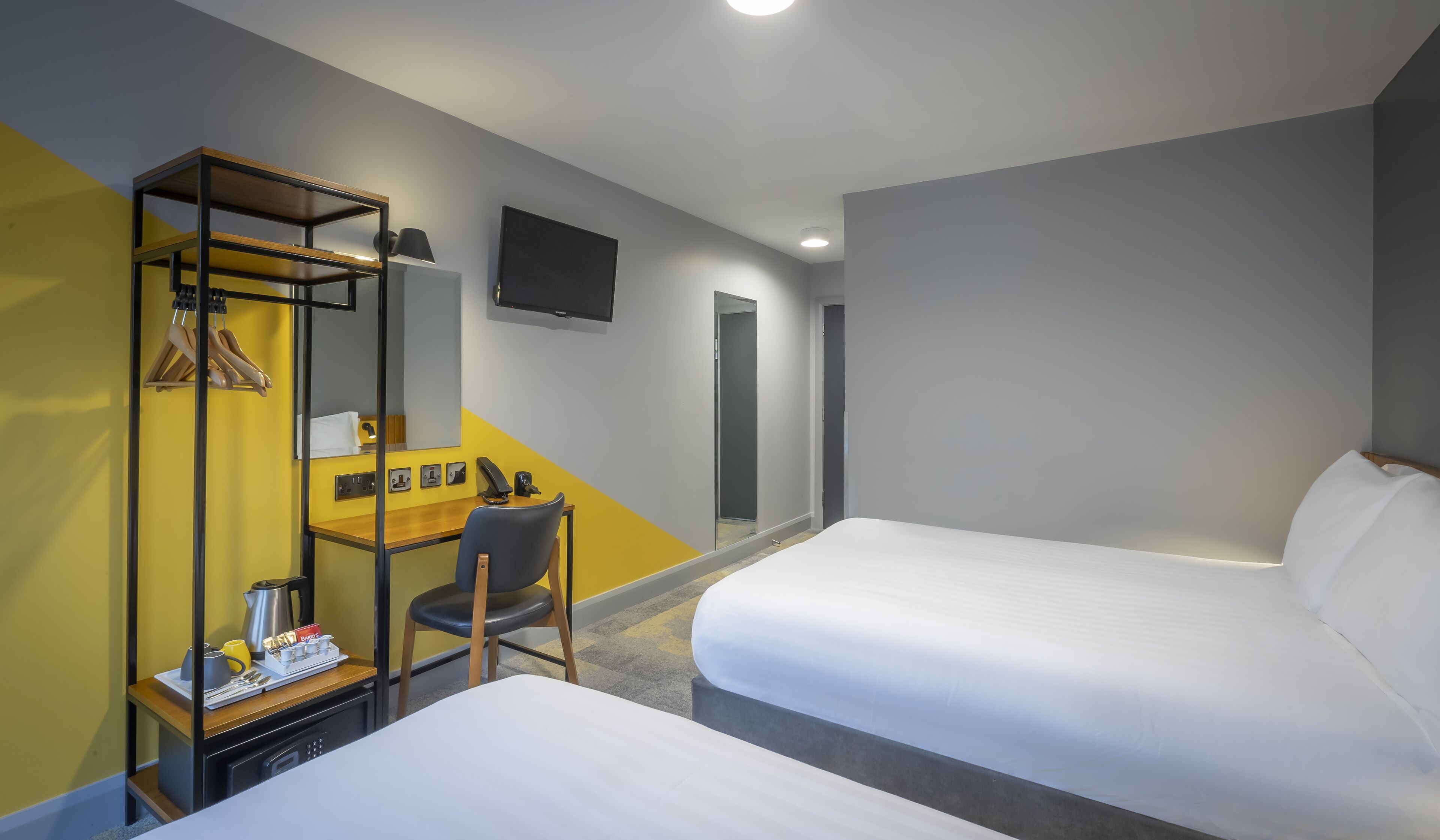 A hotel room with two beds, a desk with a chair, a wardrobe, and a flat-screen TV on the wall.