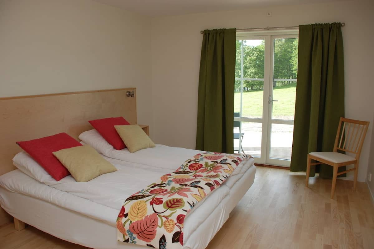 A bedroom with a bed, two pillows, a chair, and a window with curtains.