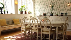 A dining area with a round table and chairs, a bench with cushions, and potted plants on a windowsill.