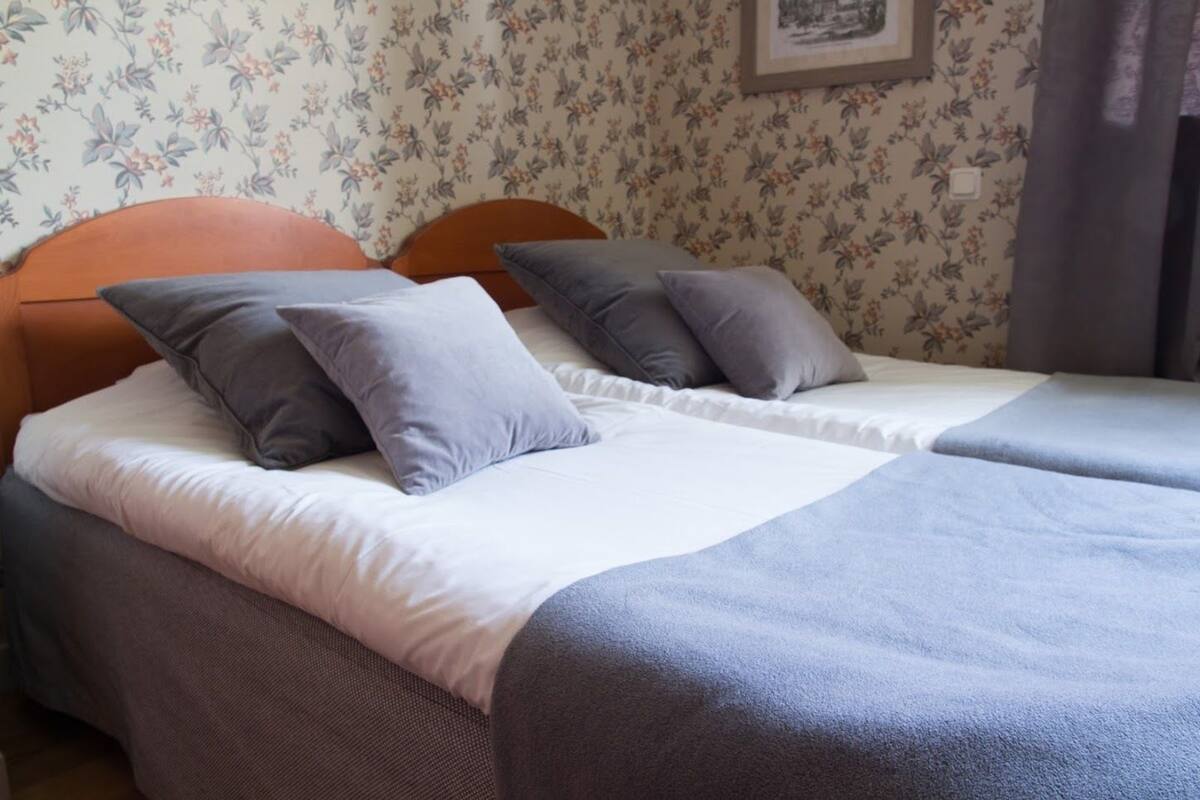 A double bed with a white and grey bedspread, two grey pillows, and a wooden headboard.