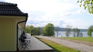 A covered outdoor seating area with tables and chairs, overlooking a lake and trees.