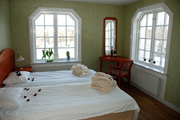 A bedroom with two beds, a desk, a chair, and large windows.