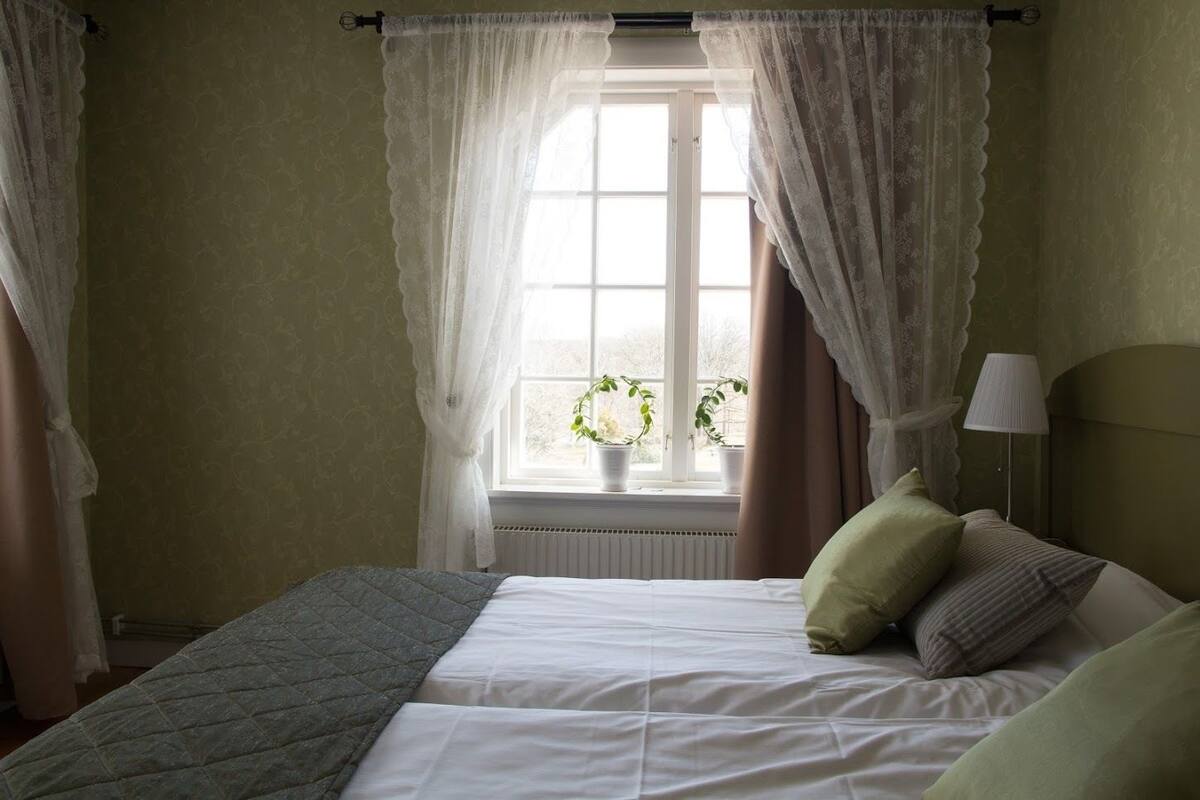 A bedroom with a bed, a window with curtains, a lamp, and a potted plant.