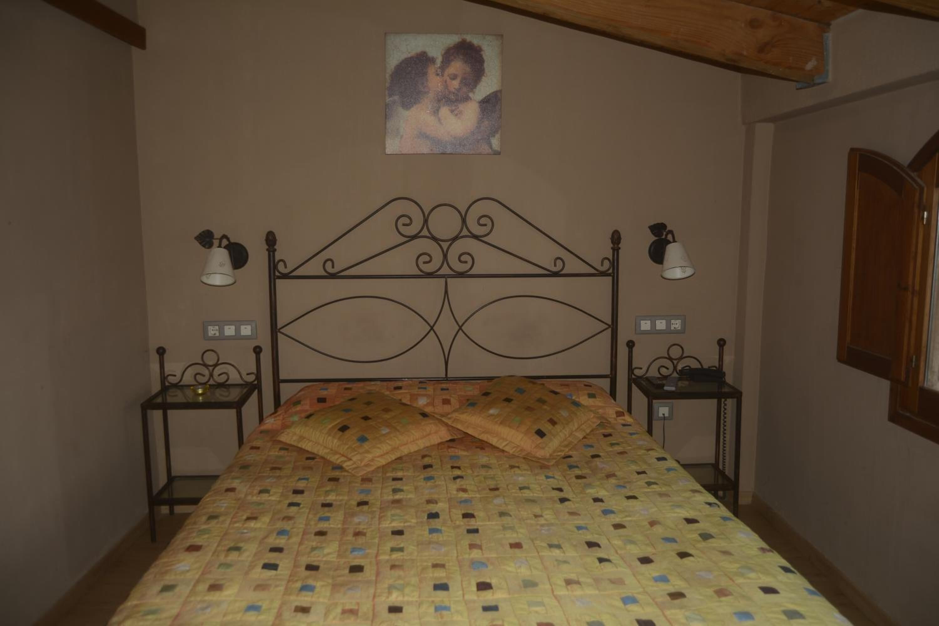 A bedroom with a metal bed frame, two bedside tables, a wall-mounted lamp, and a painting above the bed.