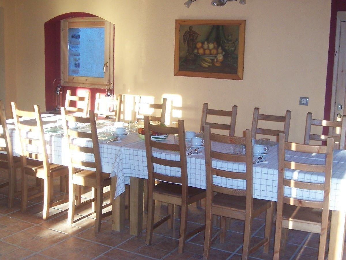 Un comedor con sillas y mesas de madera, una ventana con vistas, y un cuadro en la pared.